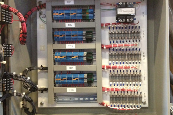Electrical control panel showing fuse blocks, terminal blocks, neat wire organization, and a transformer for industrial alarm and feedback systems.